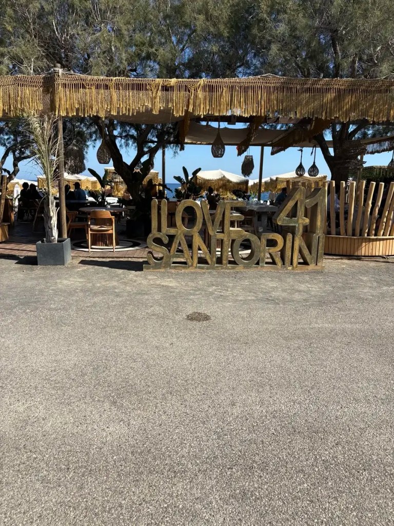 Entrance to 41 Santorini beach venue with shaded seating and a large Love 41 Santorini sign