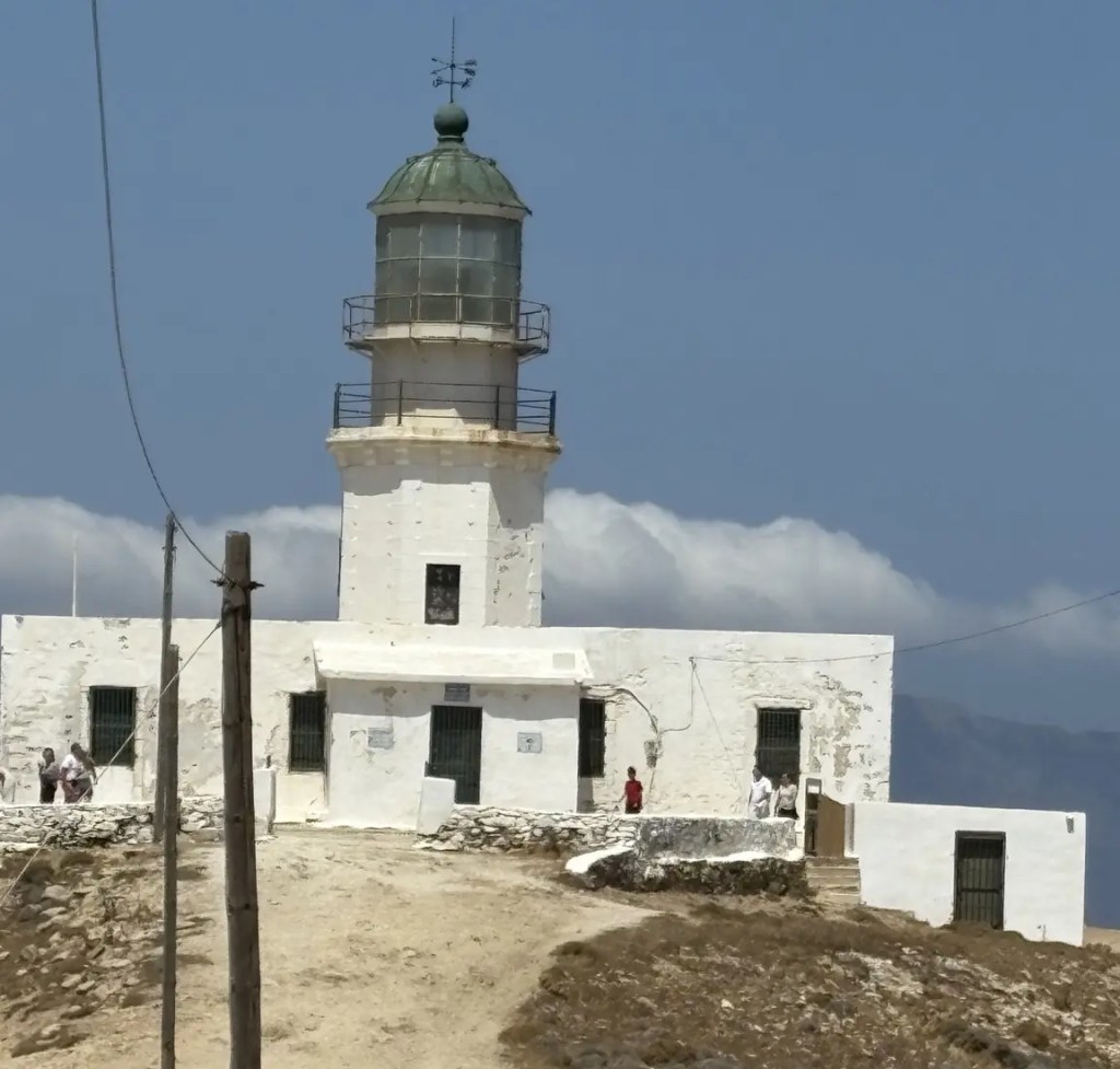 White lighthouse standing on a rocky hill beneath a bright blue sky in Mykonos