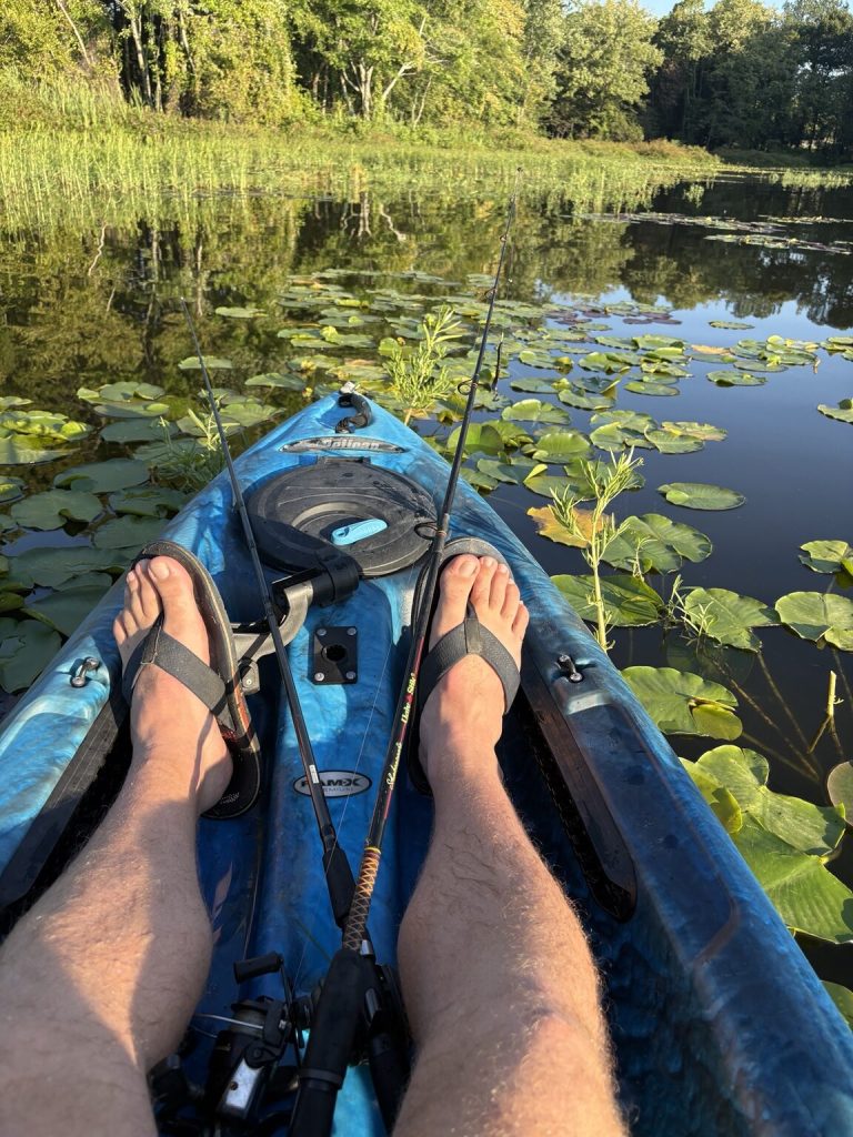 View from a blue fishing kayak surrounded by lily pads on the calm water of Beaverfork Lake