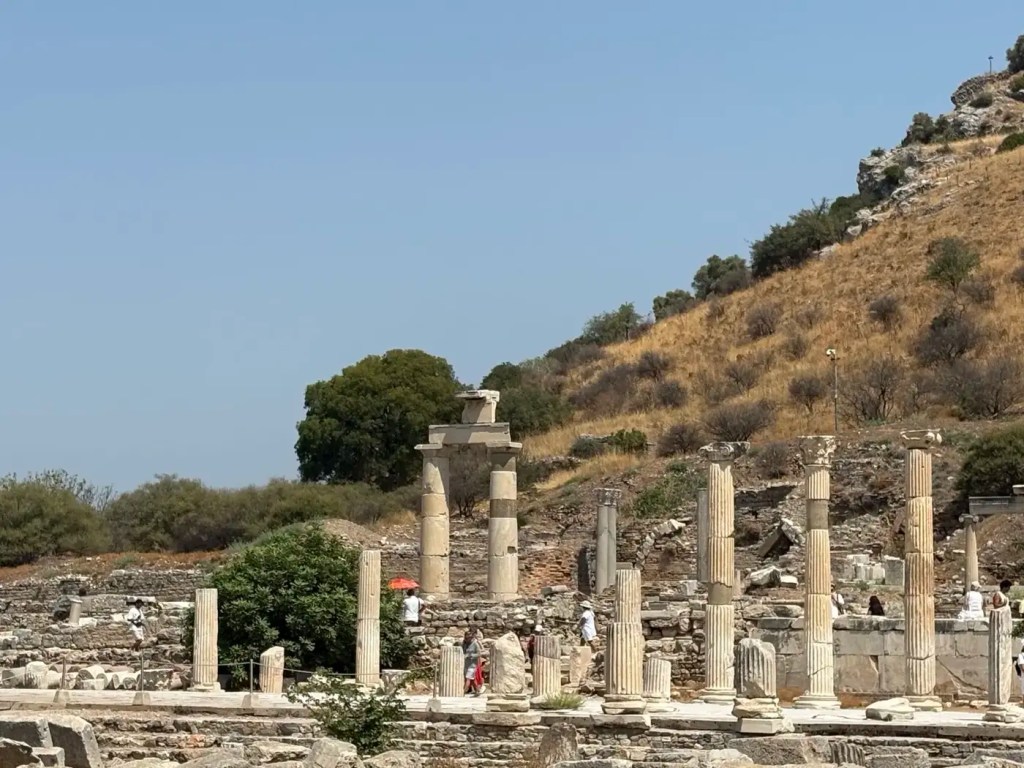 Standing stone columns and excavated ruins on a dry hillside in ancient Ephesus