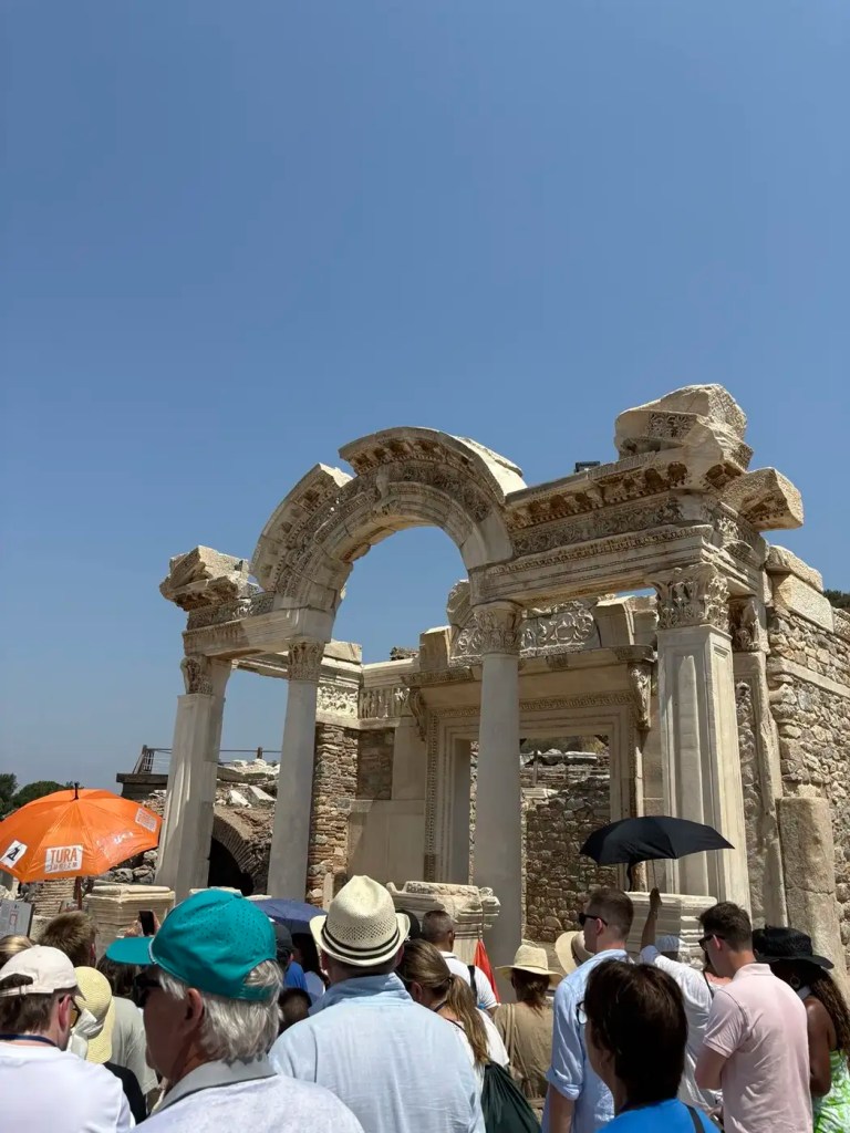 Visitors moving through a monumental ancient stone gateway at the crowded Ephesus archaeological site