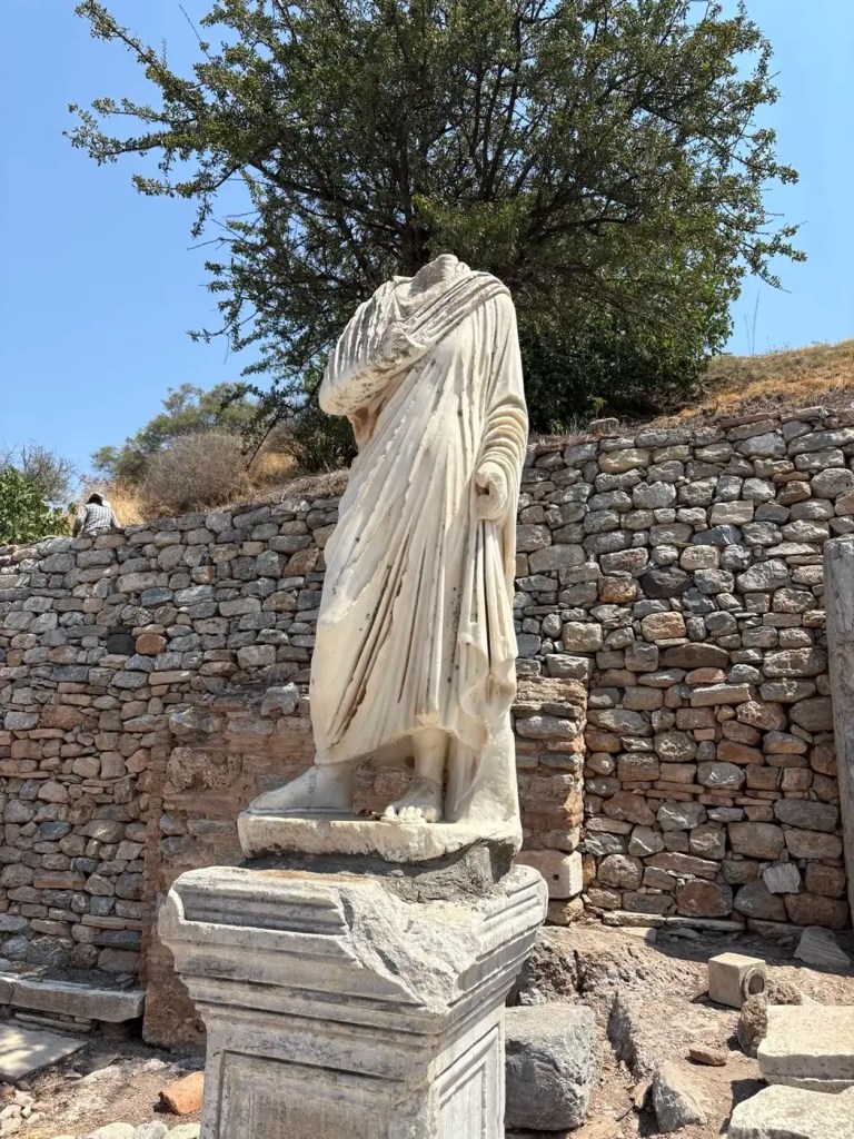 Headless marble statue standing on a pedestal among stone ruins at Ephesus