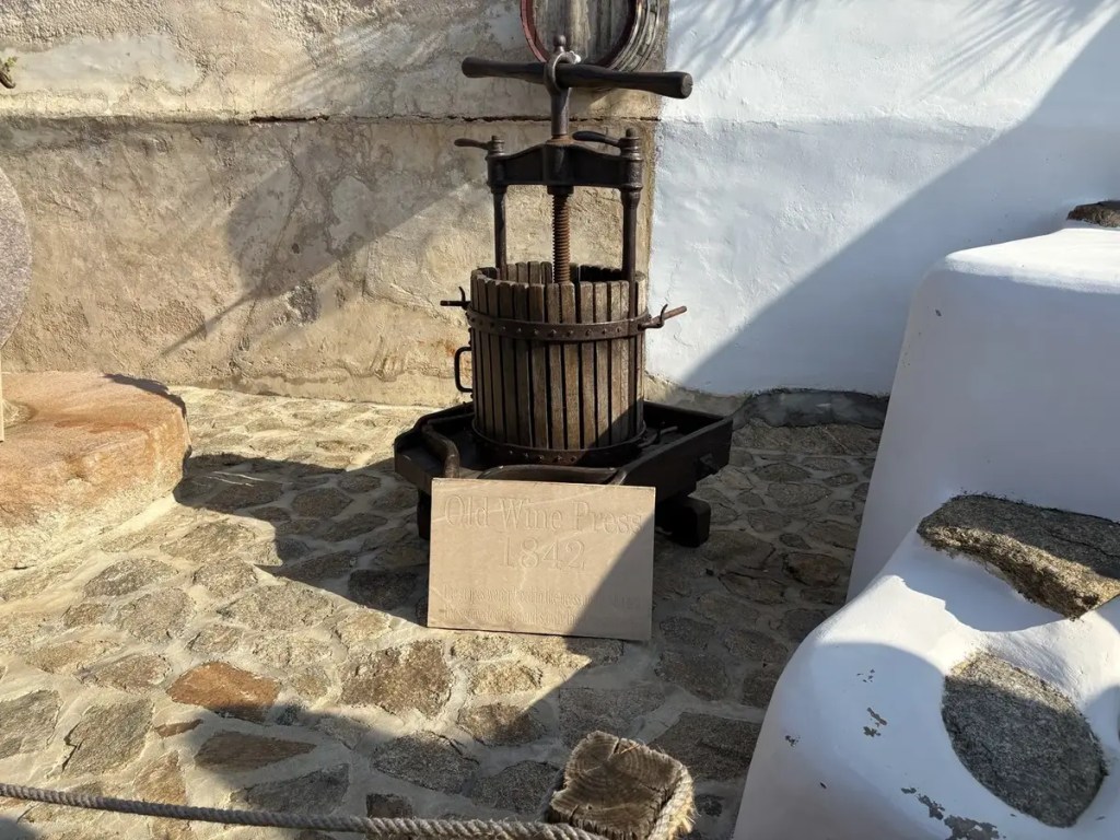 Historic wooden wine press dated 1842 displayed against whitewashed walls in Mykonos