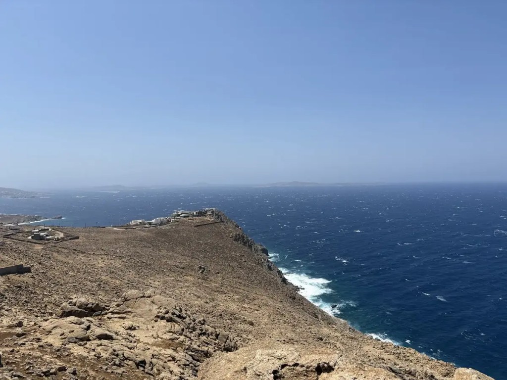 Rocky cliffs descending into the deep blue Aegean Sea under a clear sky in Mykonos