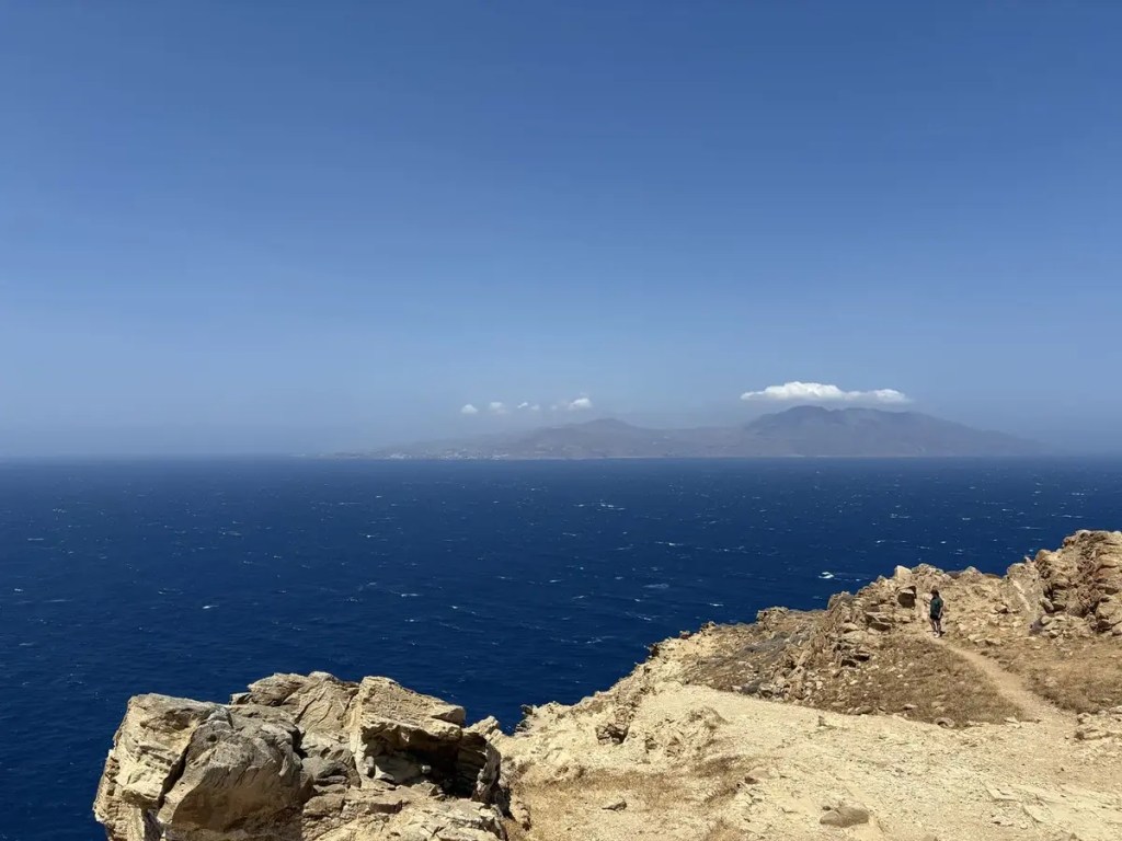 Deep blue Aegean Sea and a distant mountainous island viewed from the rocky coast of Mykonos