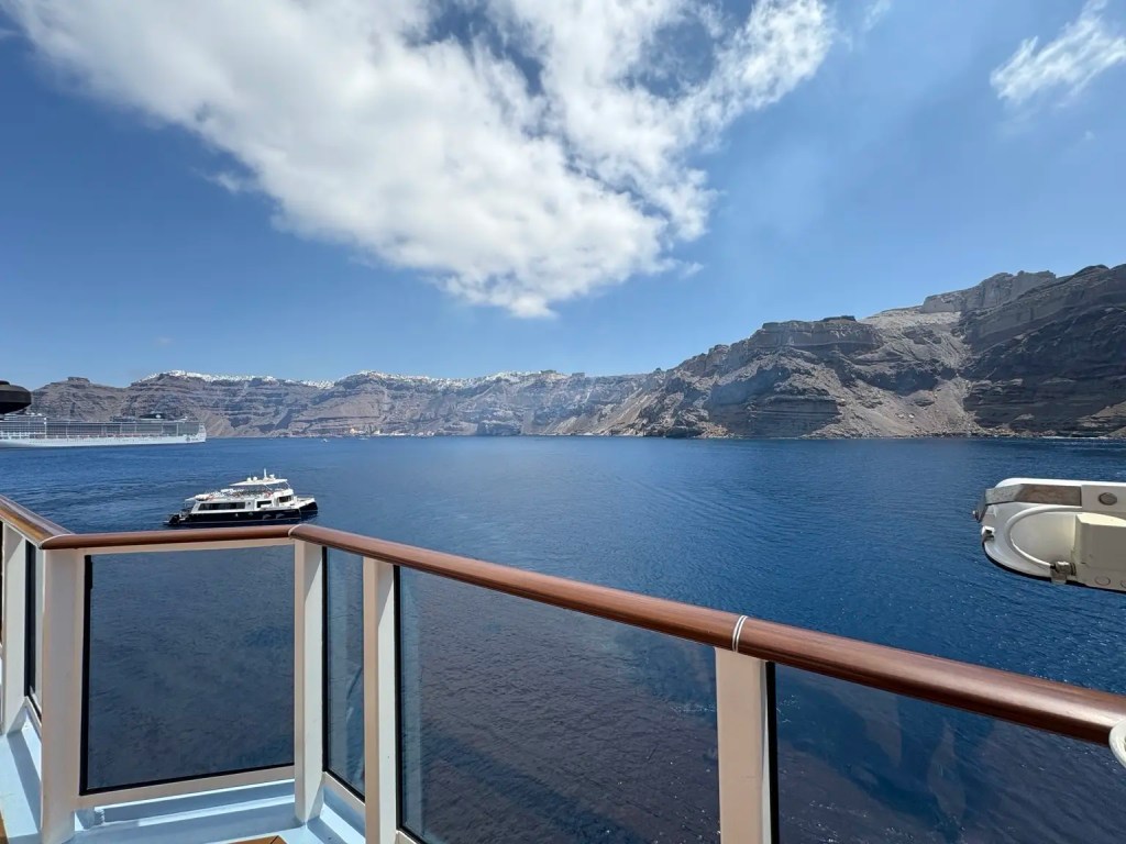 View of Santorini’s volcanic caldera cliffs and blue Aegean water from a cruise ship balcony