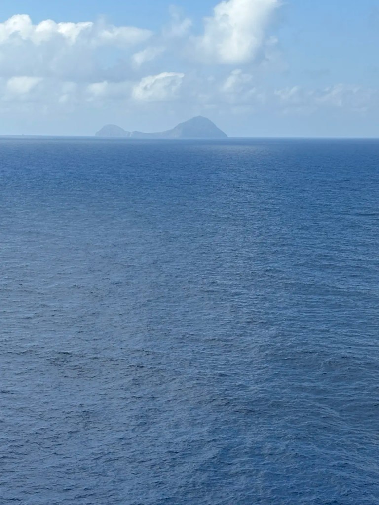 Dark volcanic island rising from the blue Aegean Sea near Santorini