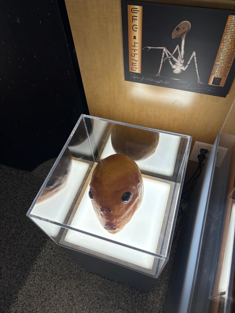 Alien head model in an illuminated museum display case.