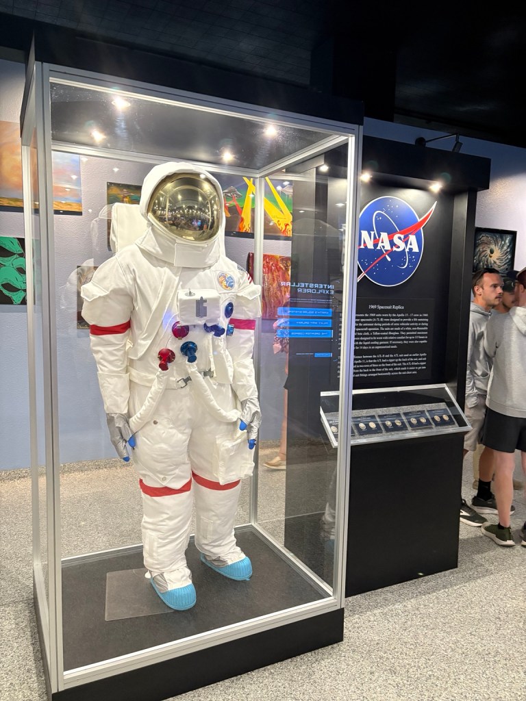White replica spacesuit in a glass museum display case beside a NASA sign.