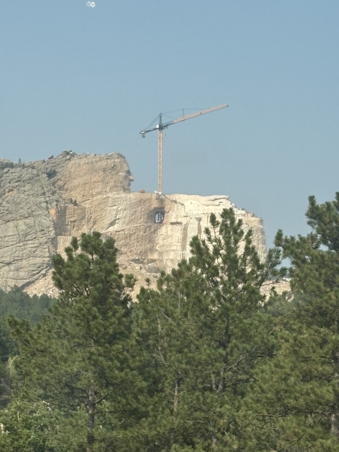 The unfinished Crazy Horse mountain carving and a construction crane above pine trees.