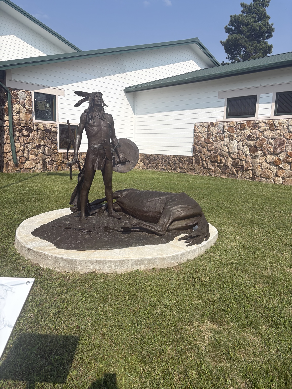 An outdoor sculpture depicting a standing figure beside a fallen bison.